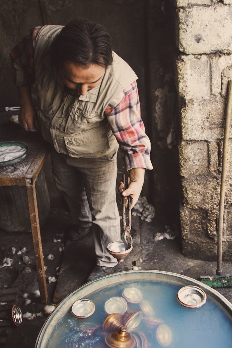 Photo Of A Man Taking Dishes Out Of A Barrel Filled With Water