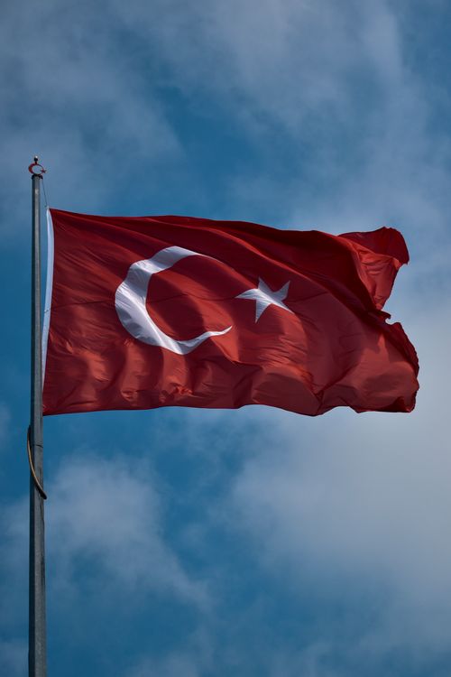 Free A vibrant red Turkish national flag waving against a clear blue sky on a tall flagpole. Stock Photo