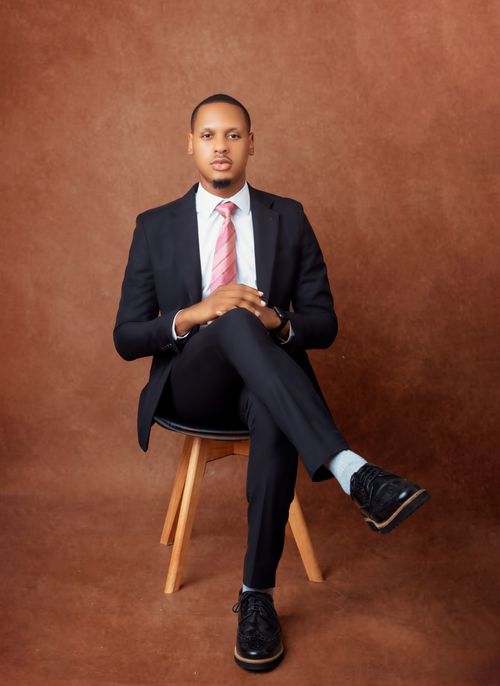Free Confident African American man in a black suit, sitting on a chair in a studio setting. Stock Photo