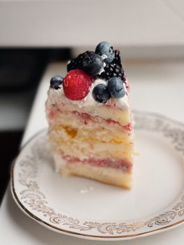 Close-up of a delicious berry chantilly cake slice with frosting and fresh fruits on an ornate plate.