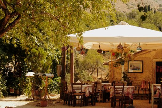 Charming outdoor seating at a Grecian tavern in Perithia, Greece, surrounded by lush greenery.