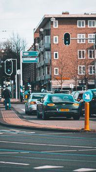 A vibrant city street with luxury cars, traffic lights, and urban architecture in daylight.