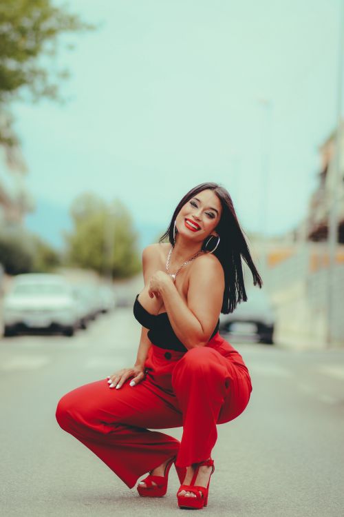 Free Fashionable woman in red pants and heels confidently posing on an urban street with a bright smile. Stock Photo