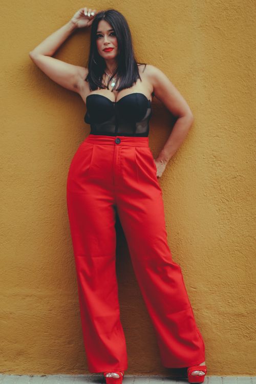 Free Fashion-forward woman posing in red pants and black top against a vibrant yellow wall. Stock Photo