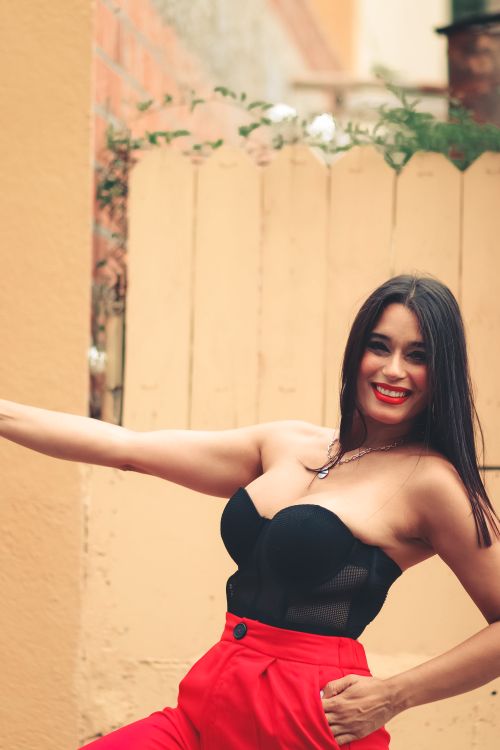 Free Young woman with red lipstick smiling and posing outside in stylish black and red outfit. Stock Photo