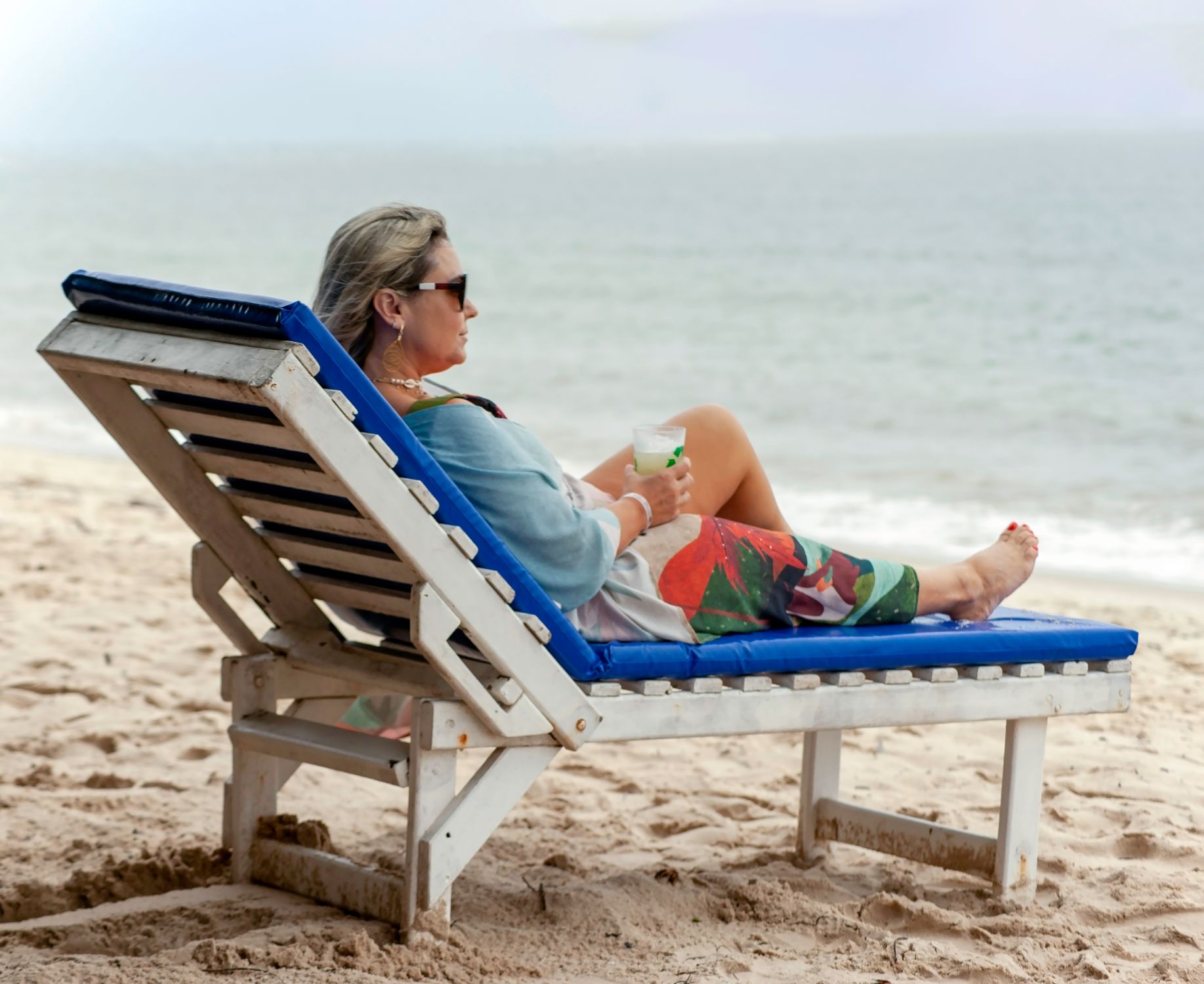 Woman enjoying a relaxing moment on a beach lounge chair while holding a refreshing drink by the shore