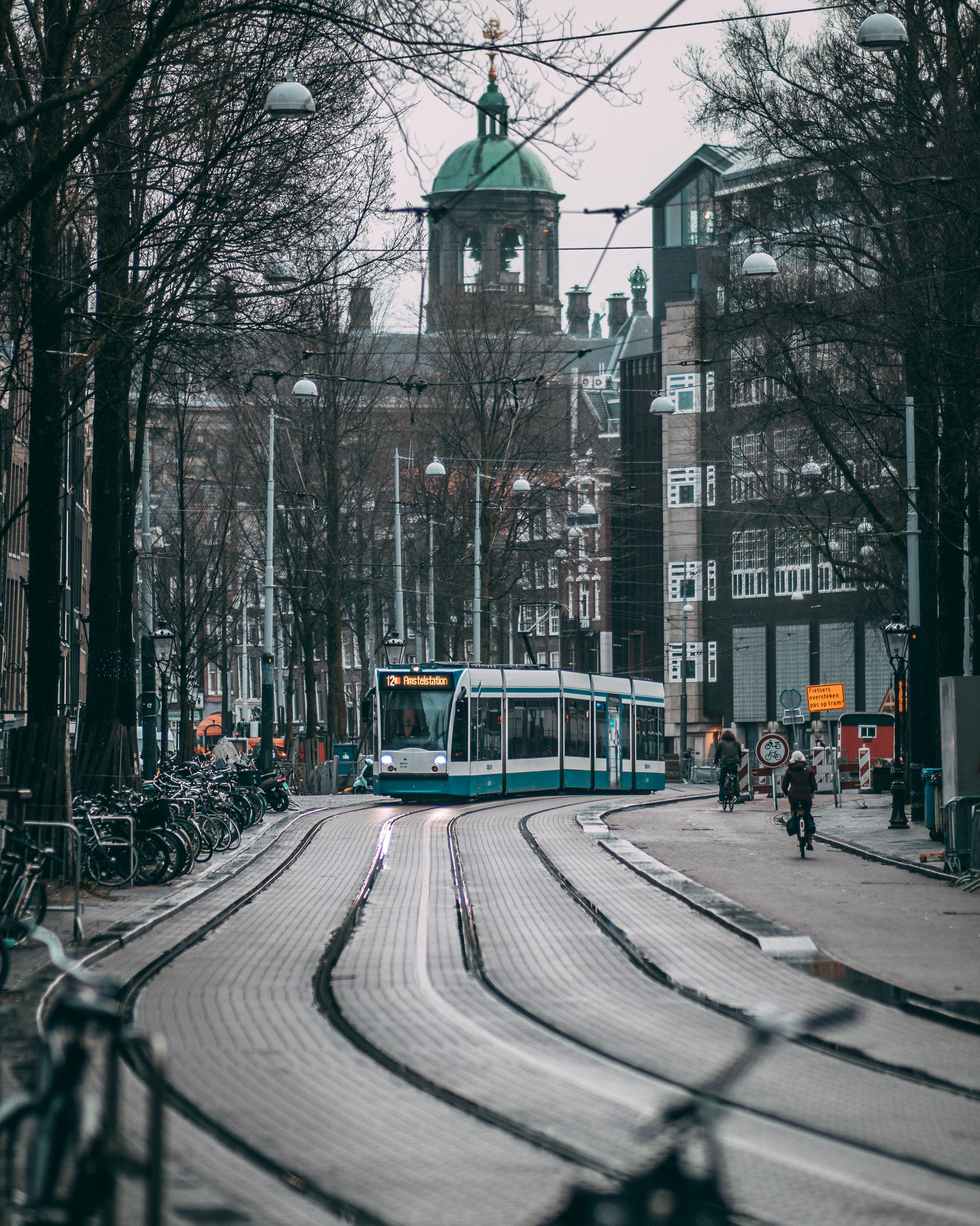 Free Urban Amsterdam view featuring a tram passing through a lively street in winter, surrounded by classic architecture. Stock Photo