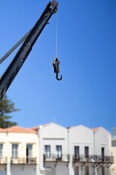 A crane hook against a blue sky with the traditional architecture of Rethimnon, Greece.