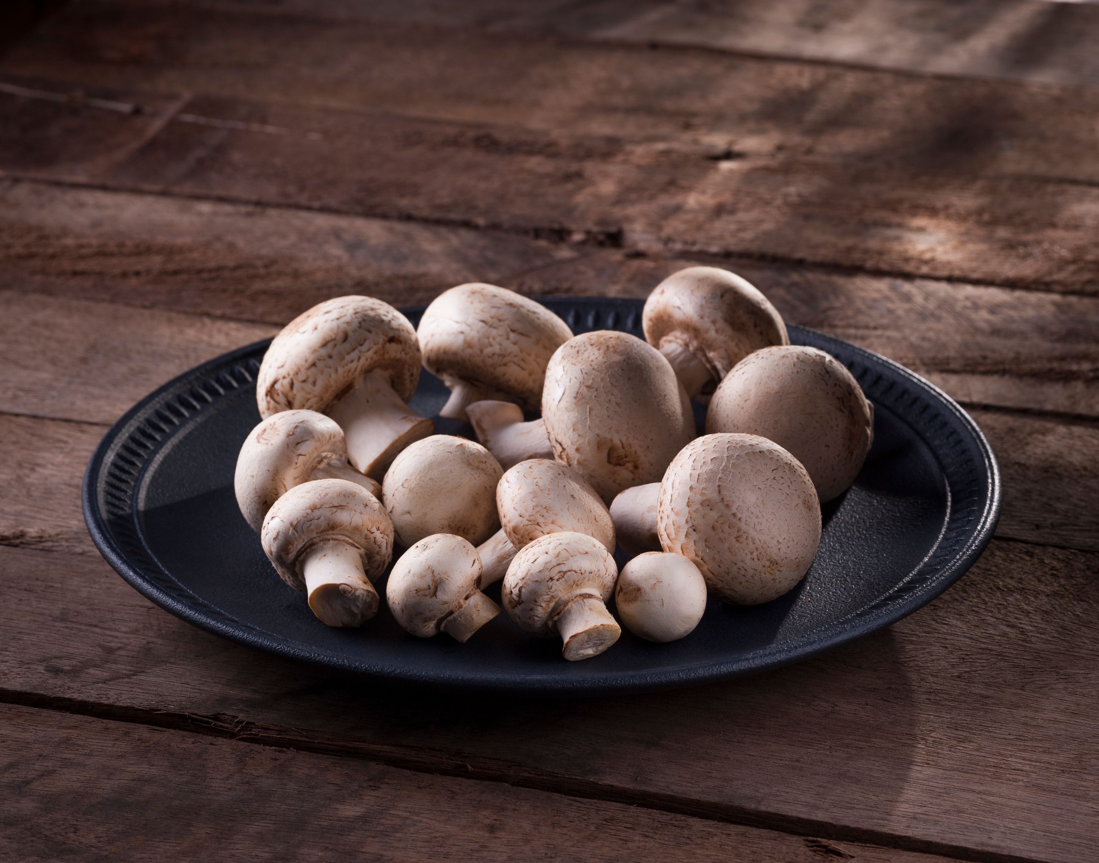 A black plate filled with fresh white mushrooms on a rustic wooden table.