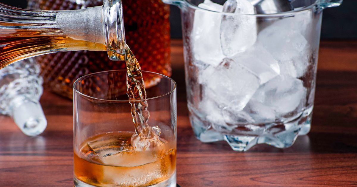 A close-up of whiskey being poured into a glass with ice, perfect for cocktail imagery.