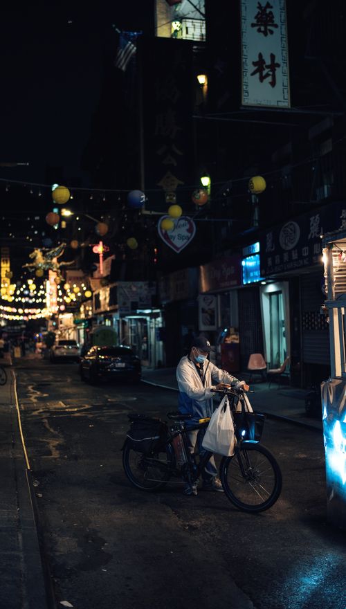 Free A man with a bicycle on a lively urban street at night, surrounded by lights. Stock Photo