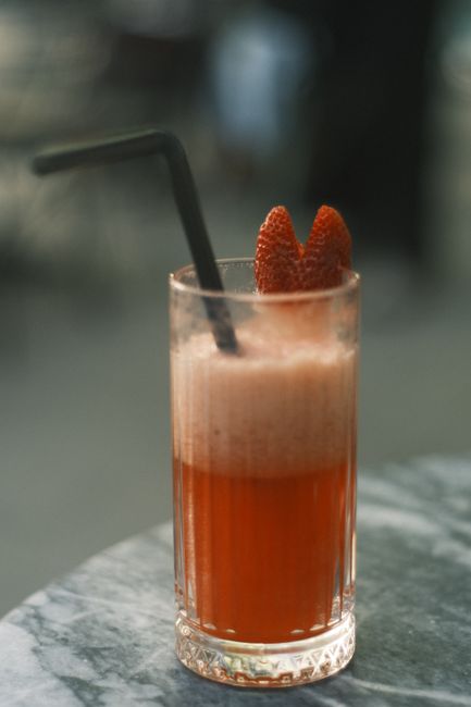 A glass of frothy strawberry juice with a straw and garnished strawberries.