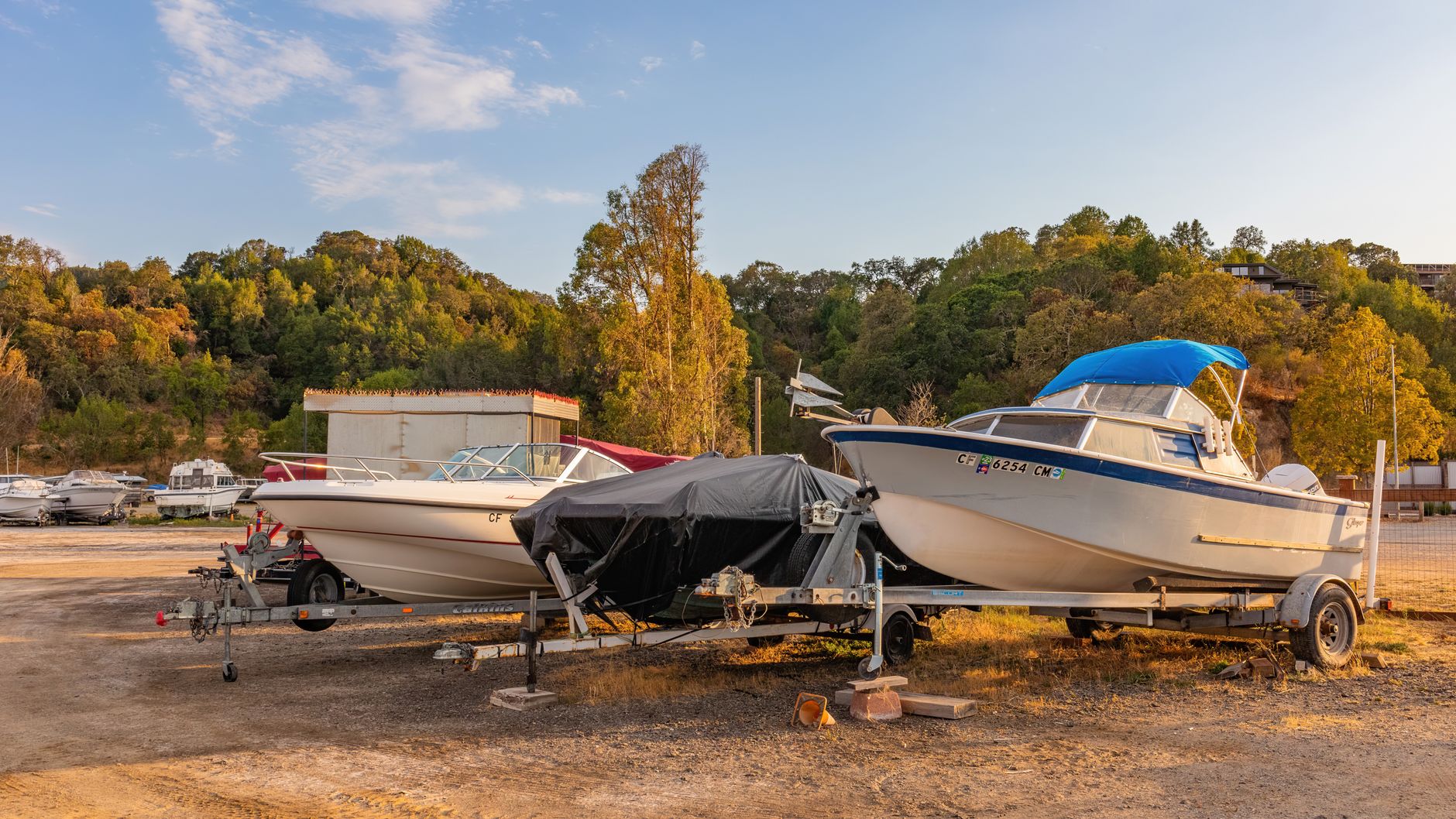Boat trailers parked in a storage lot at sunset, showing trailer couplers and frames that require safety chains