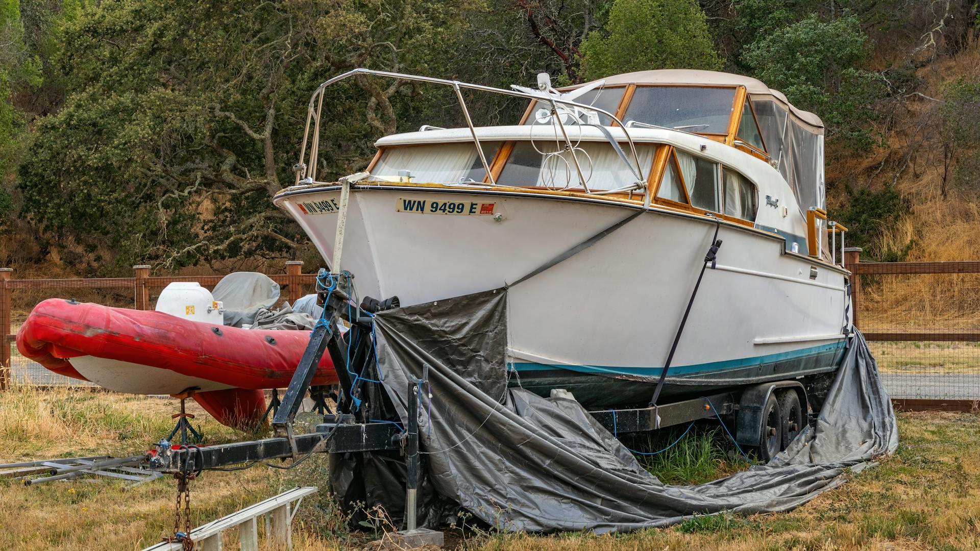 A white yacht on a trailer beside a red inflatable boat, set outdoors.
