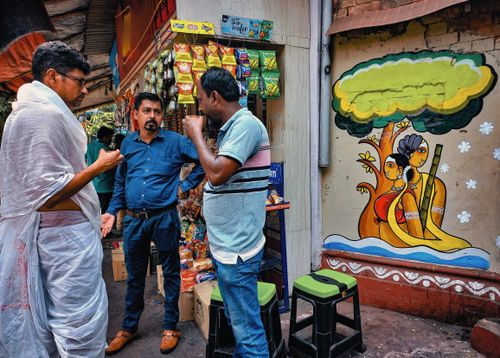 Free Three men engaging in conversation beside a shop in Kolkata, featuring traditional Indian wall art. Stock Photo