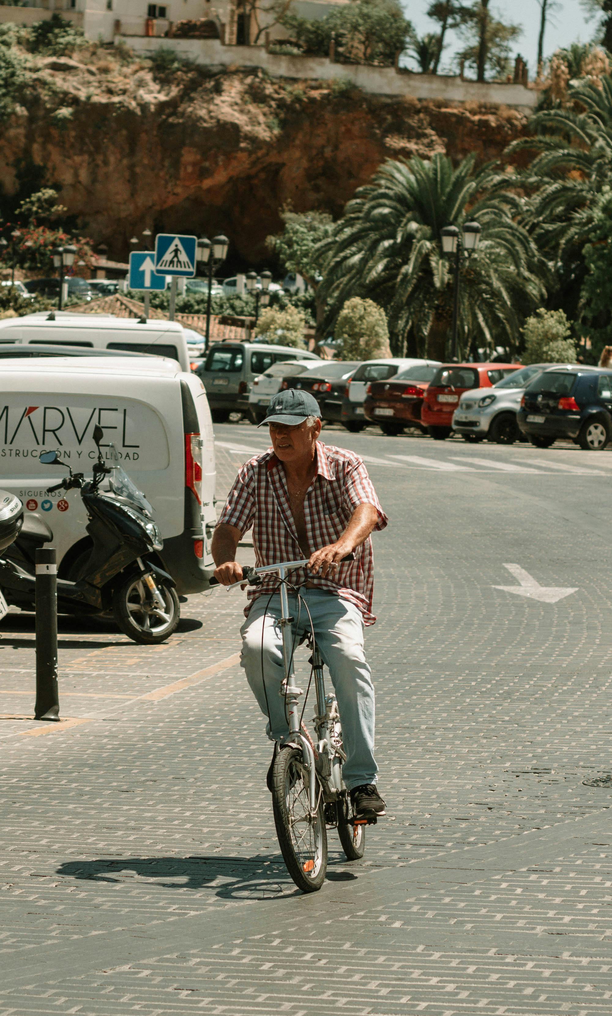 Man leisurely riding bicycle on a sunny street, surrounded by parked cars and palm trees.