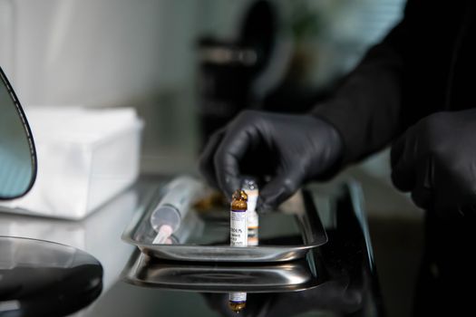 Close-up of gloved hands arranging medicine vials on a tray in a clinical setting.
