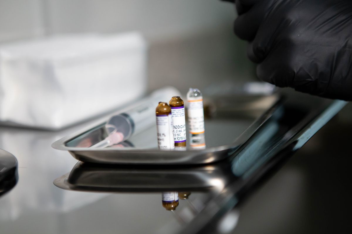 Three small injection vials and a syringe on a steel tray with a black-gloved hand beside them
