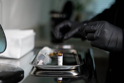 A Person Wearing Black Gloves Beside a Vial on Stainless Tray