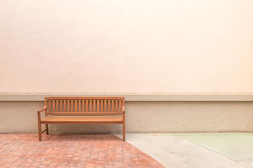 Free Wooden bench positioned against a neutral plaster wall, creating a minimalist and serene outdoor setting. Stock Photo
