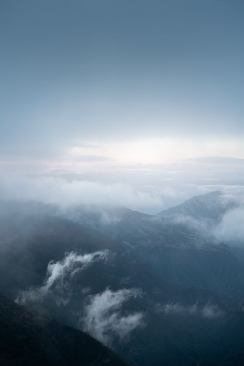 Free A serene view of mountains shrouded in misty clouds at dawn, creating a tranquil and ethereal atmosphere. Stock Photo