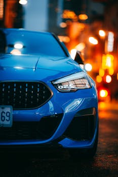 Close-up of a sleek blue car parked at night with vibrant city lights.