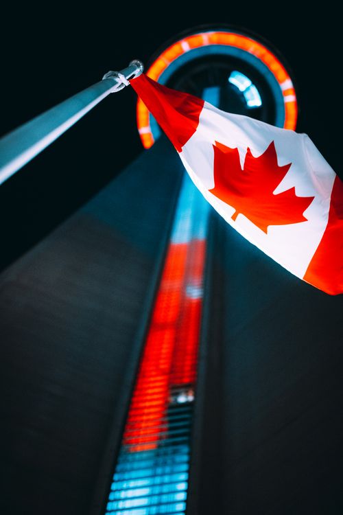 Free A night view of the CN Tower with a Canadian flag illuminated against the night sky. Stock Photo