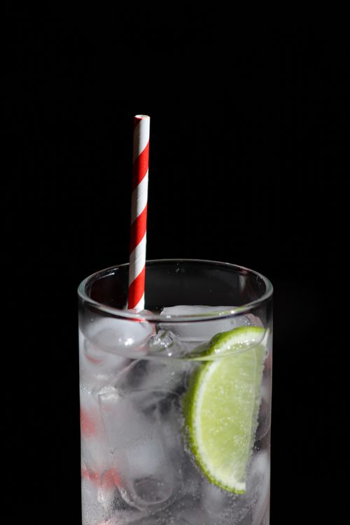 Free Close-up of a cool drink with lime, ice, and striped straw against a black background. Stock Photo