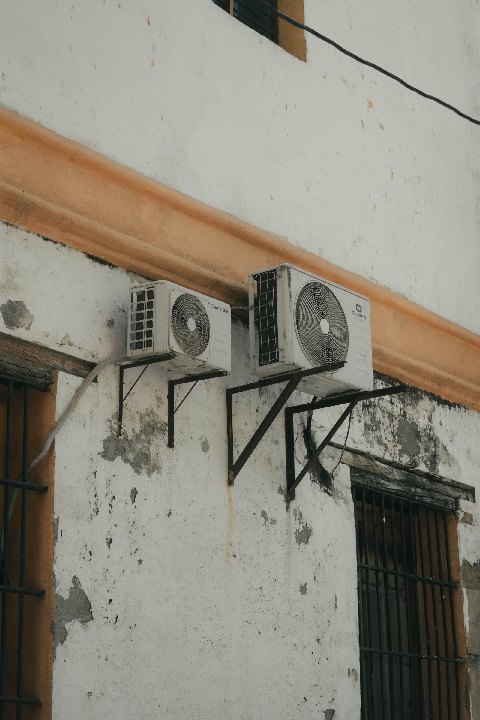 Two outdoor central air conditioner condenser units mounted on an exterior wall