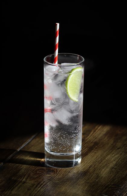 A tall glass of vodka soda with ice, a lime wedge on the rim, and visible carbonation bubbles rising through the clear drink.