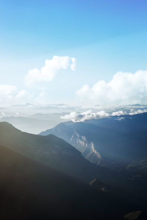 Free A breathtaking aerial view of mountains under a clear blue sky with fluffy clouds. Stock Photo