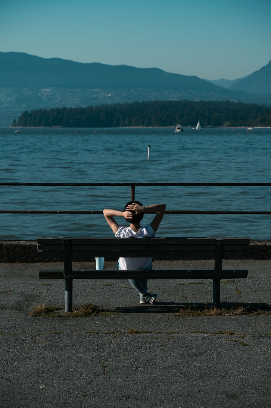 Woman on a bench by the Vancouver seawall overlooking ocean and mountains