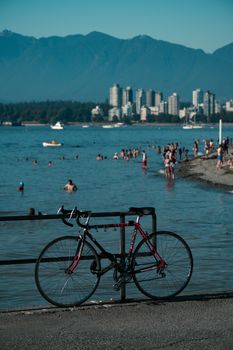 Parked bicycle overlooking English Bay, Vancouver, with swimmers and city skyline.
