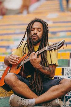 A street musician with dreadlocks plays acoustic guitar on colorful steps, creating a vibrant and lively scene.