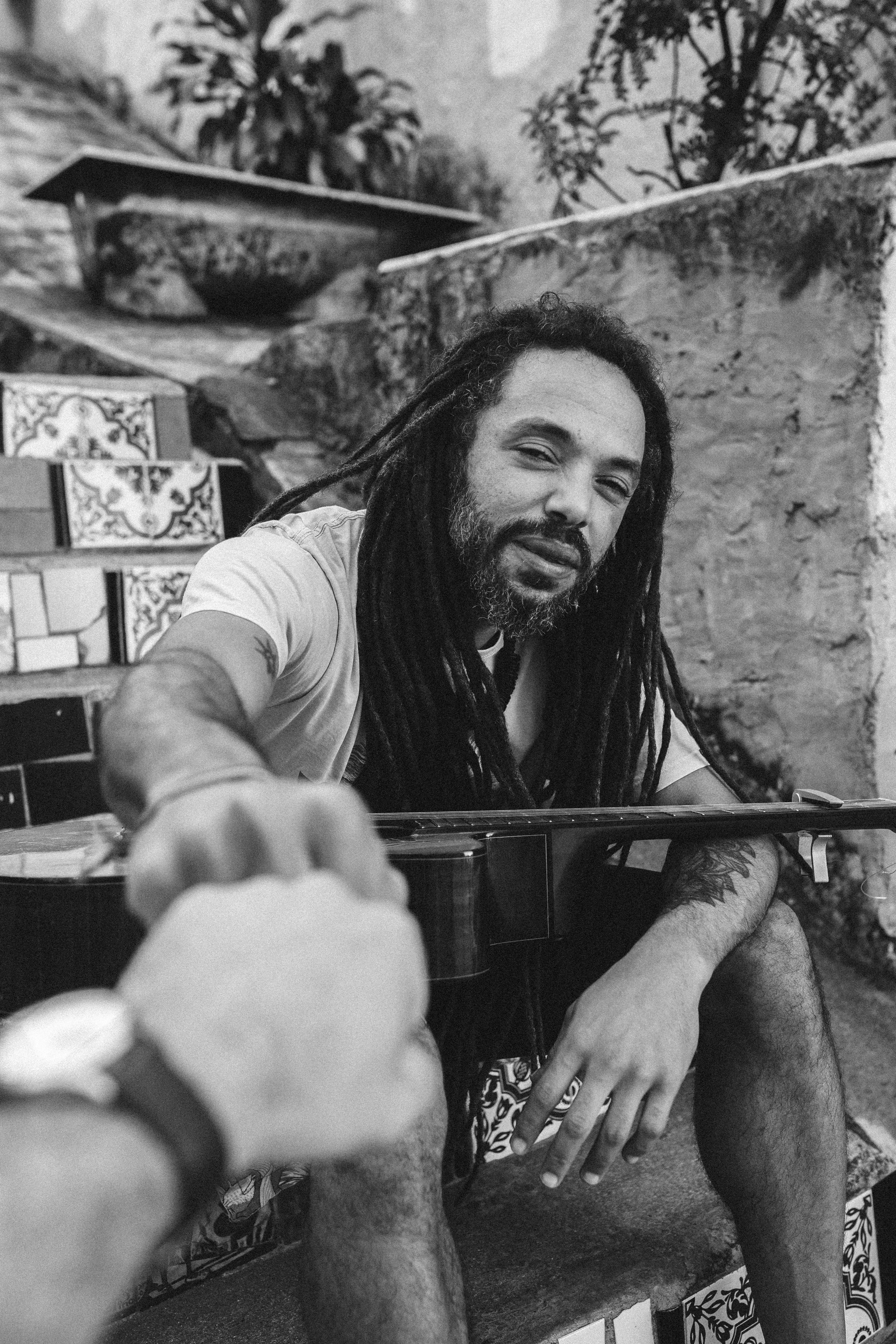Black and white photo of a bearded man with dreadlocks holding a guitar and fist bumping.