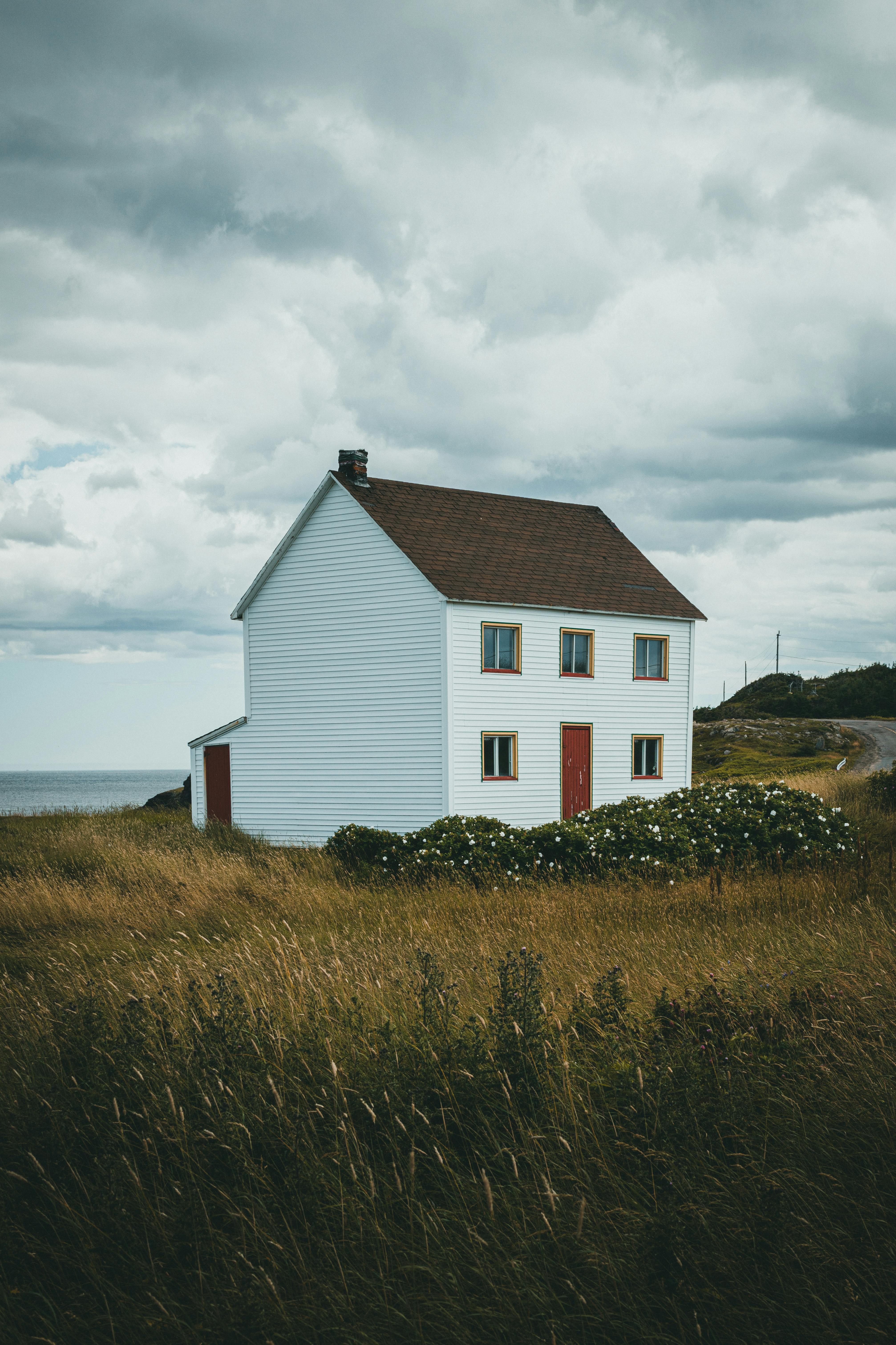 A serene countryside farmhouse surrounded by open grass fields under a cloudy sky.