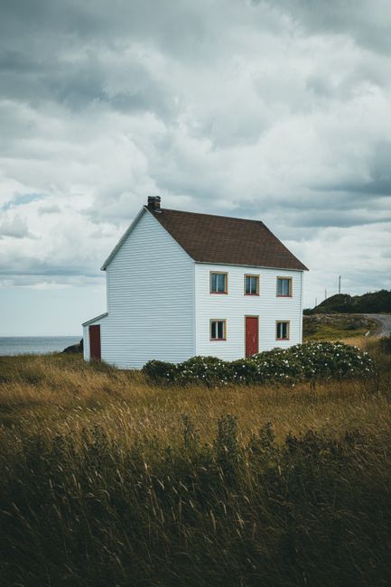 A serene countryside farmhouse surrounded by open grass fields under a cloudy sky.