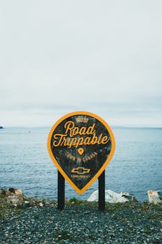 Road trippable sign on a rocky coastline with ocean background.