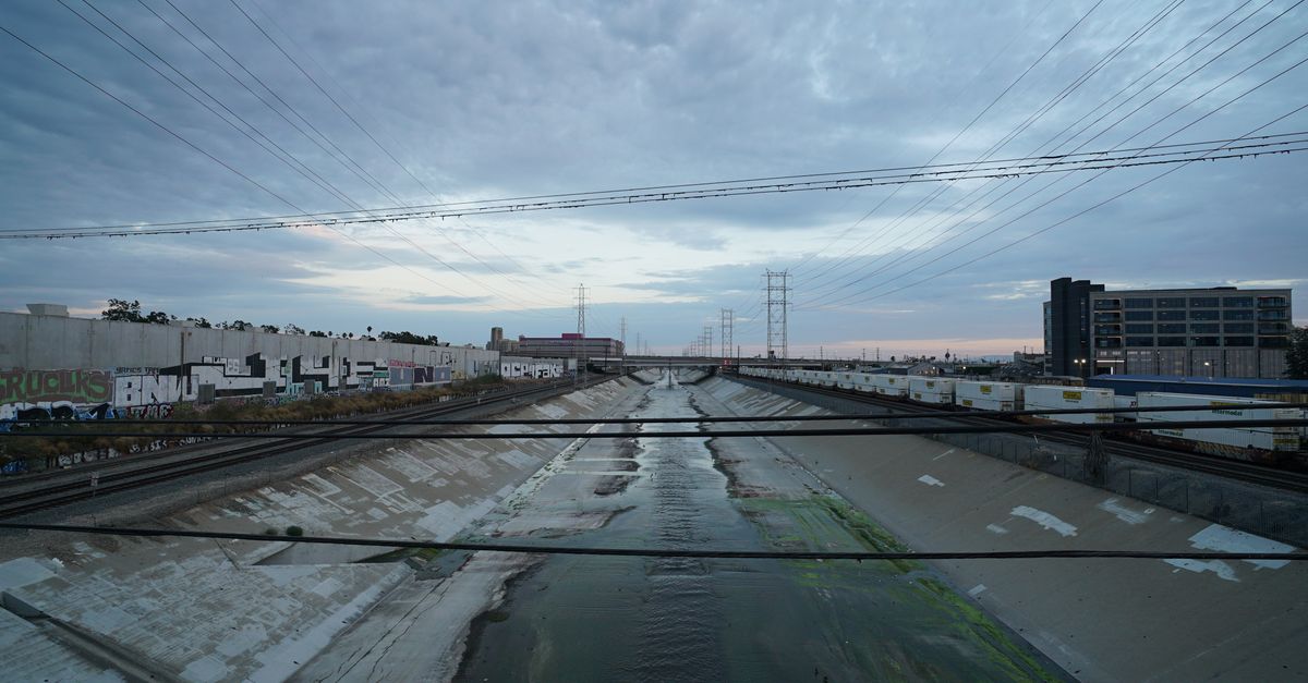 Aerial view of the Los Angeles River with urban surroundings and cloudy sky at dawn.