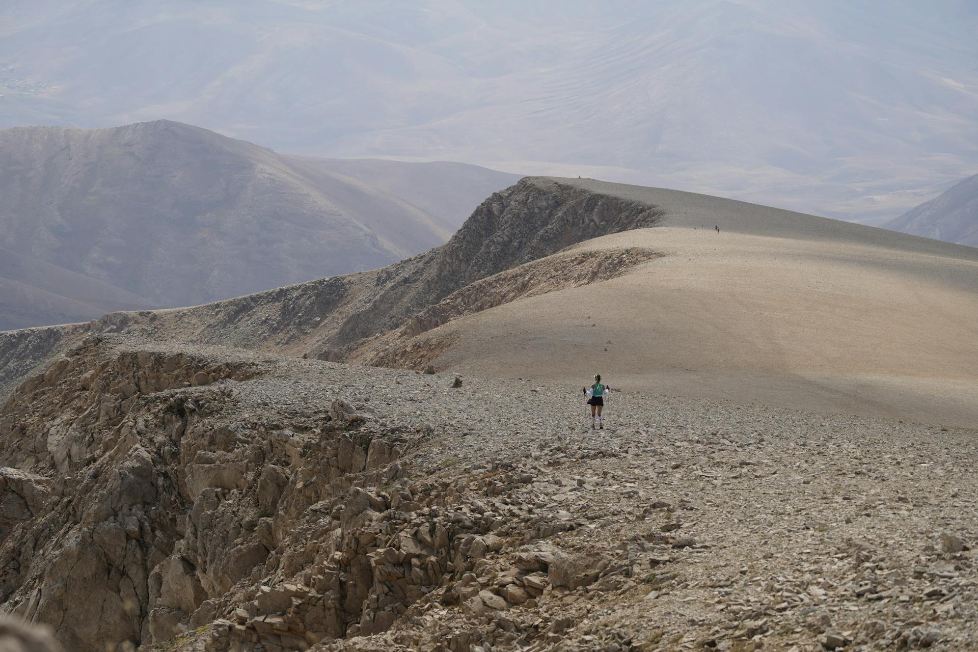 A solitary hiker traverses a rocky mountain landscape under a clear sky.