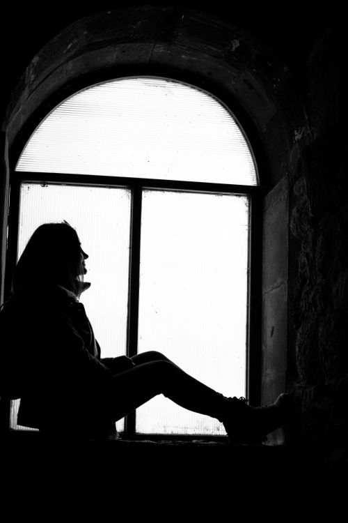 Free Artistic silhouette of a woman in profile sitting by an arched window in a black and white theme. Stock Photo