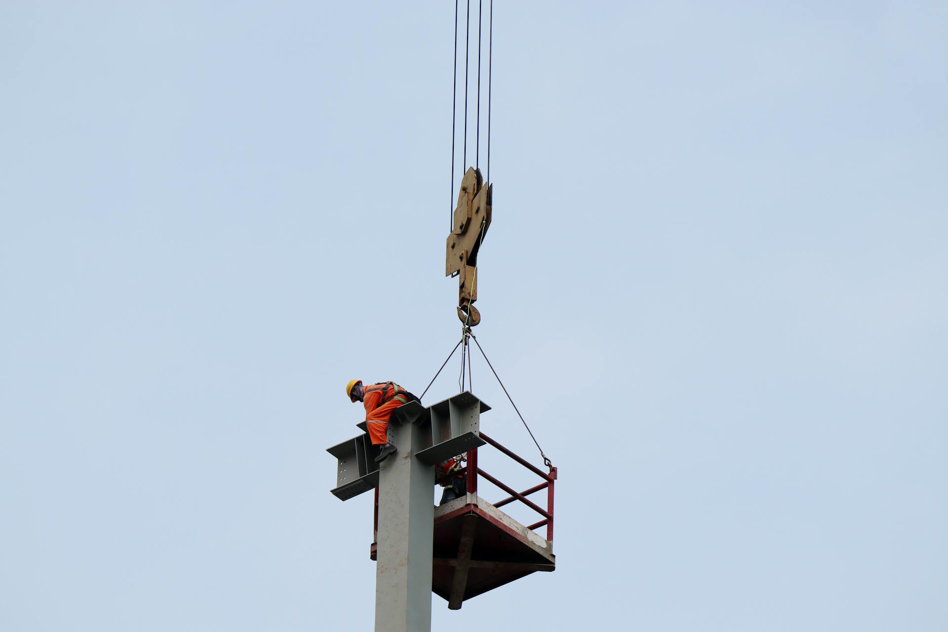 A construction worker operates at high altitude using a crane on a clear day.