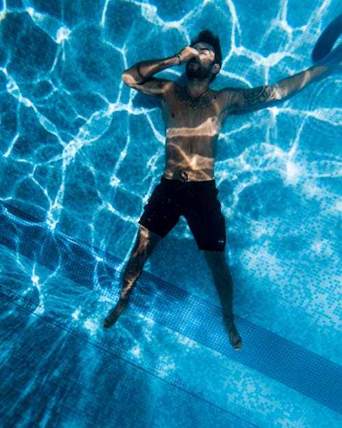 A Man Lying Down Underwater on the Swimming Pool Floor