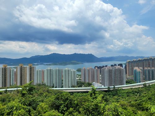 Free A breathtaking aerial view of New Territories, Hong Kong, featuring lush greenery and towering skyscrapers against mountain backdrop. Stock Photo