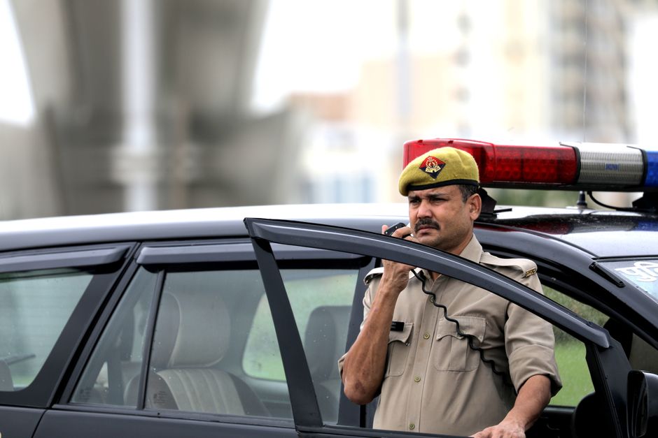 Police officer using radio near patrol car outdoors, ensuring public safety.