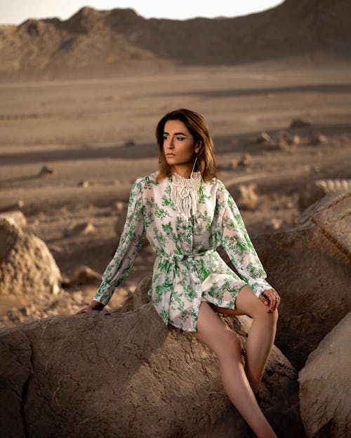 A Woman in Green and White Long Sleeve Dress Sitting on Brown Rock