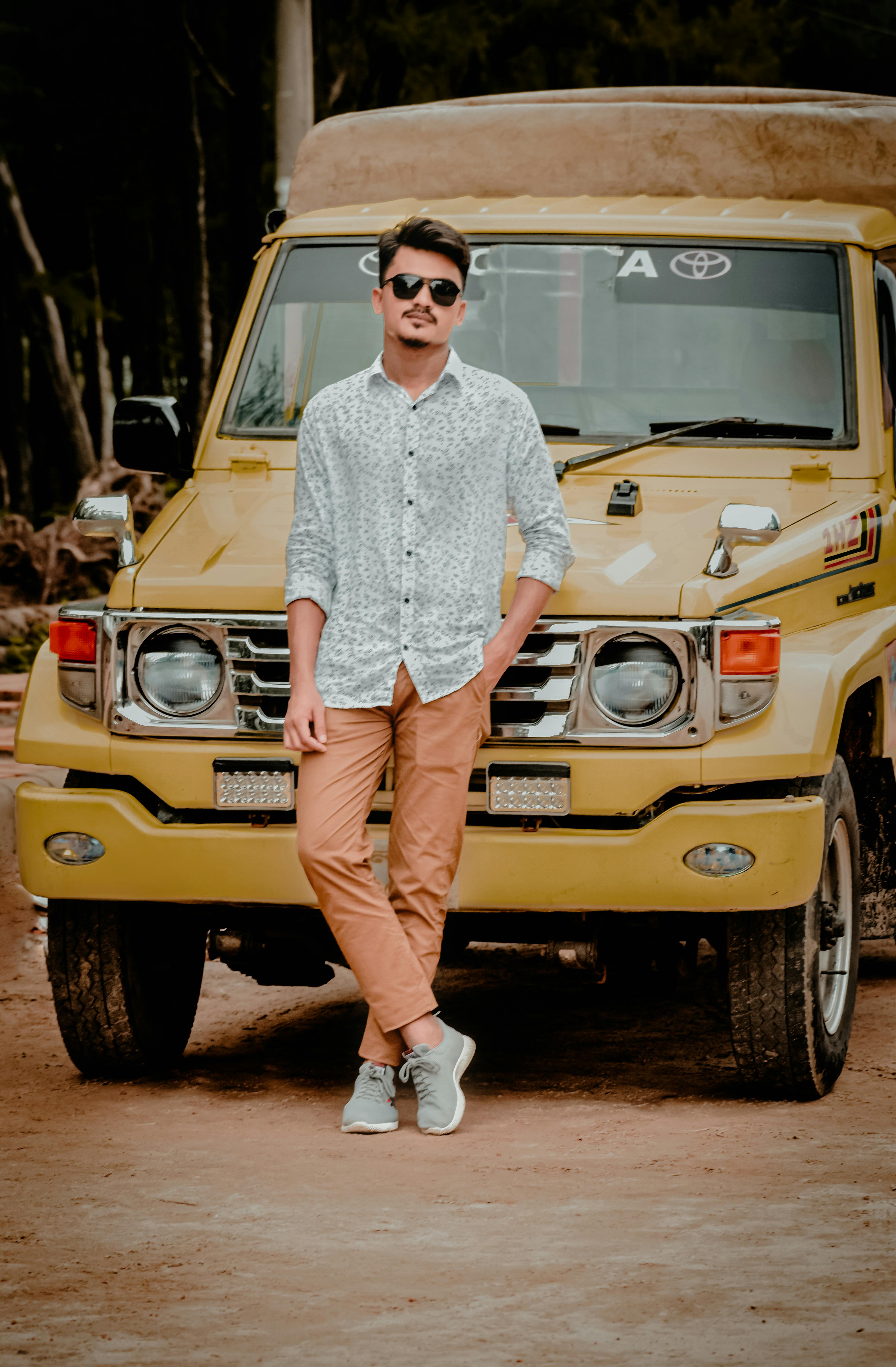 Stylish man posing in casual attire with a yellow jeep outdoors.