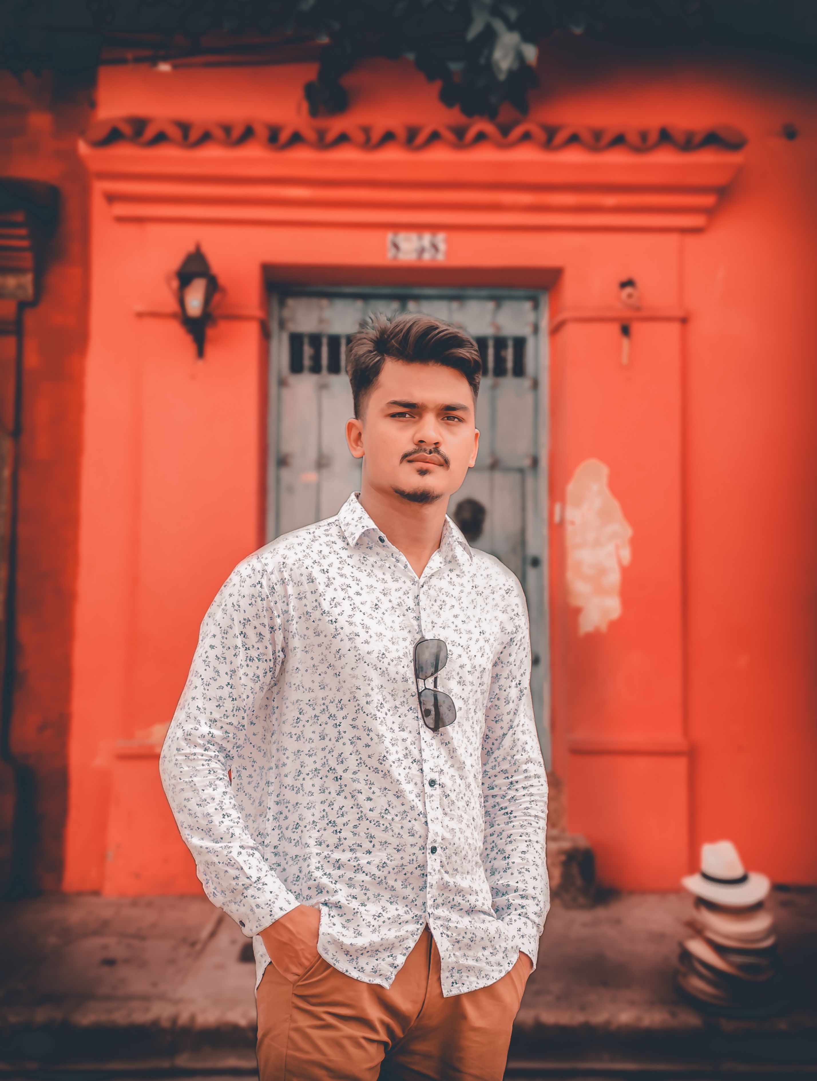 Fashionable man posing casually with hands in pockets against a vivid orange wall backdrop. Perfect for modern lifestyle themes.