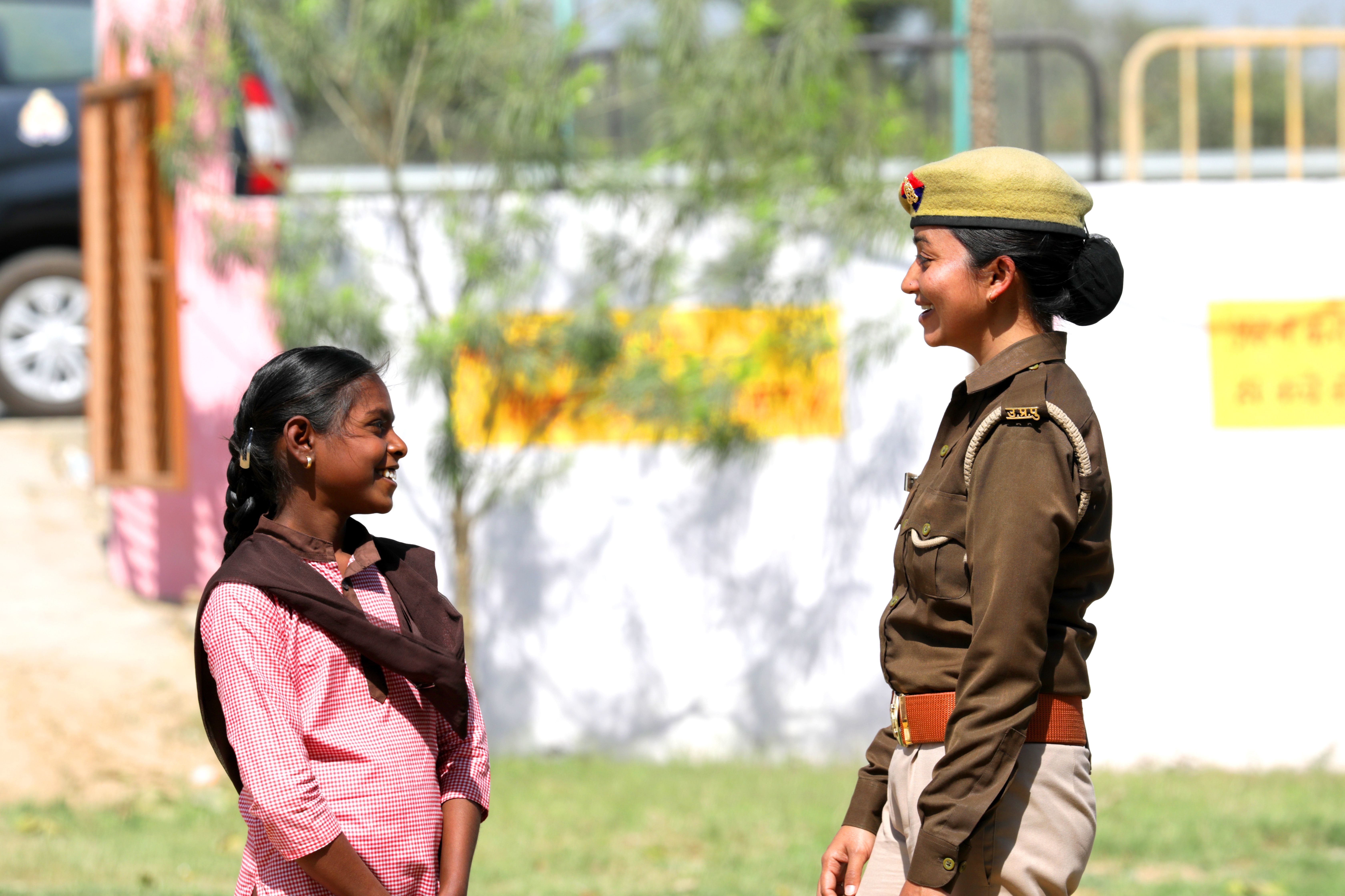 A candid outdoor interaction between a policewoman and a young girl, both smiling.