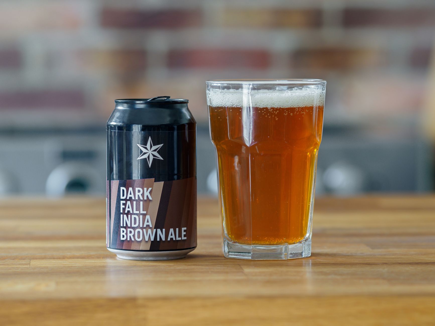 A close-up of a Dark Fall India Brown Ale can and glass on a wooden table indoors.